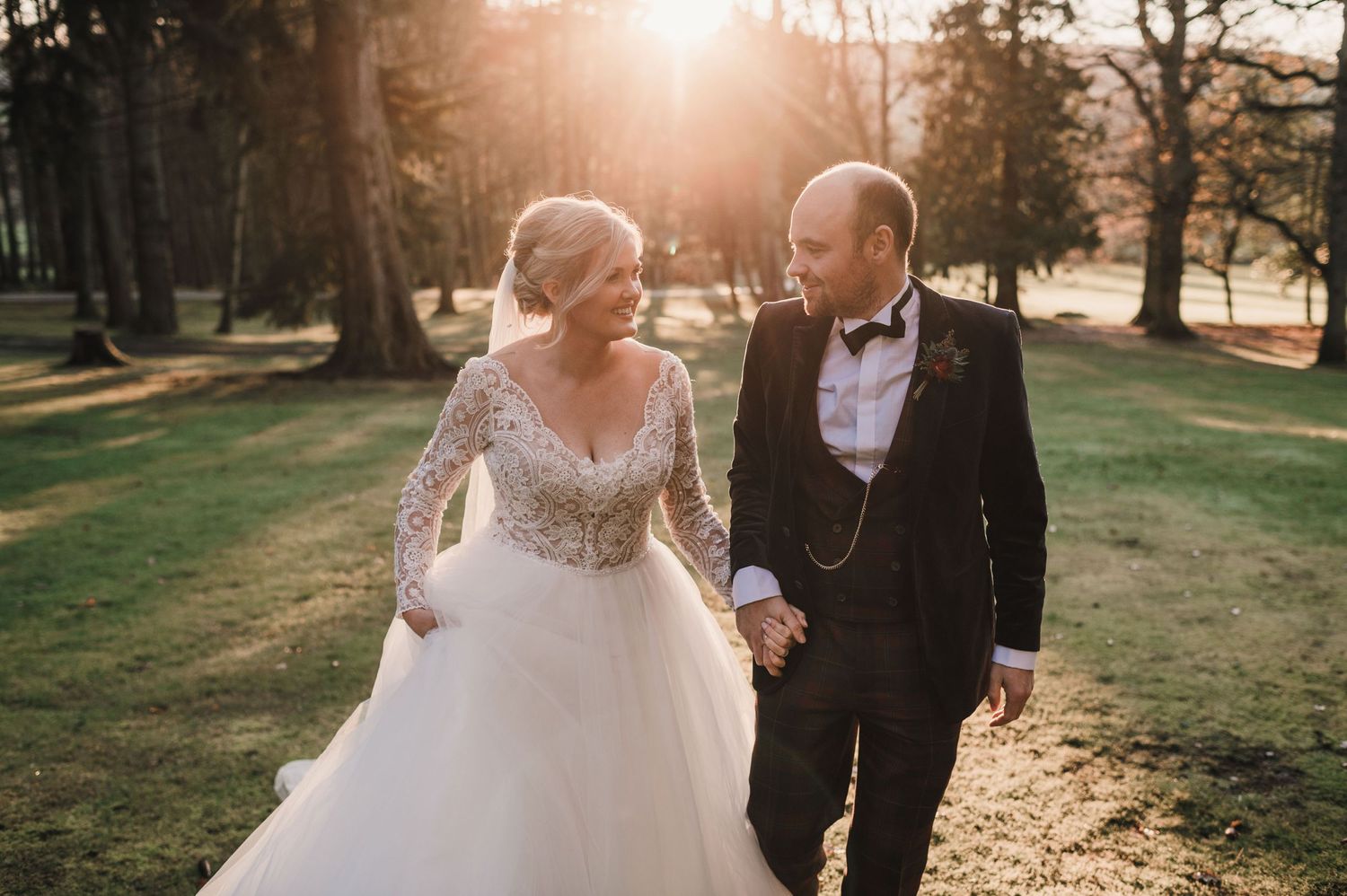 Sunset wedding portrait with couple walking through golden-lit parkland.