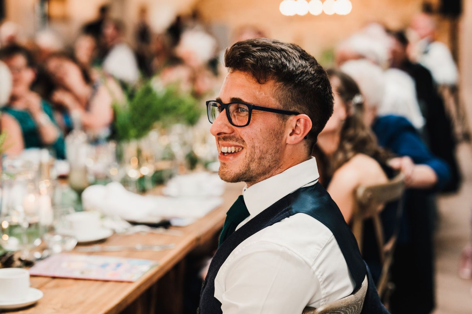 Guest in formal attire smiles during wedding reception dinner.