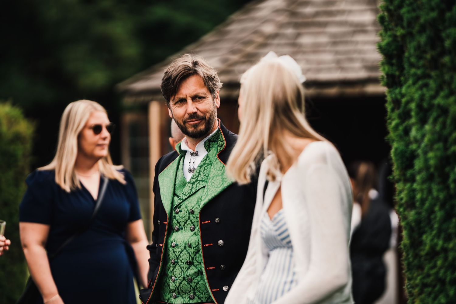 Wedding guest wearing distinctive green vest and formal attire socializing at outdoor event.