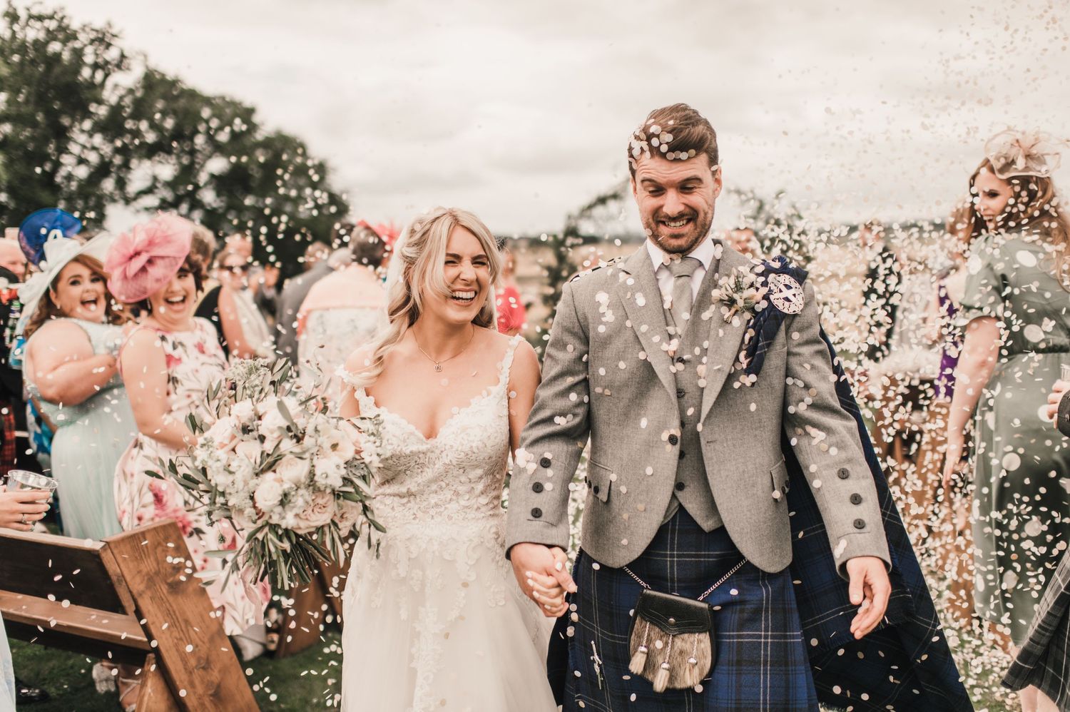 Joyful celebration with confetti at an outdoor wedding ceremony against rolling countryside.