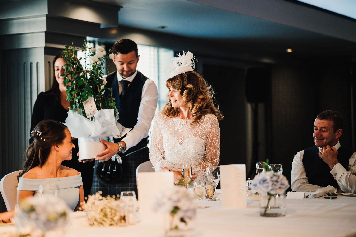 A formal wedding reception dinner with guests seated at an elegant table with floral centerpieces.