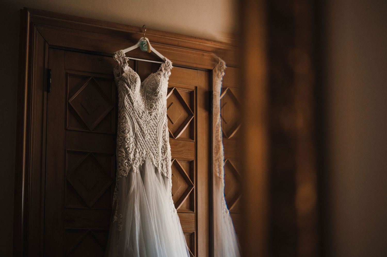 Bridal gown with detailed lace bodice displayed against wooden paneled wall.