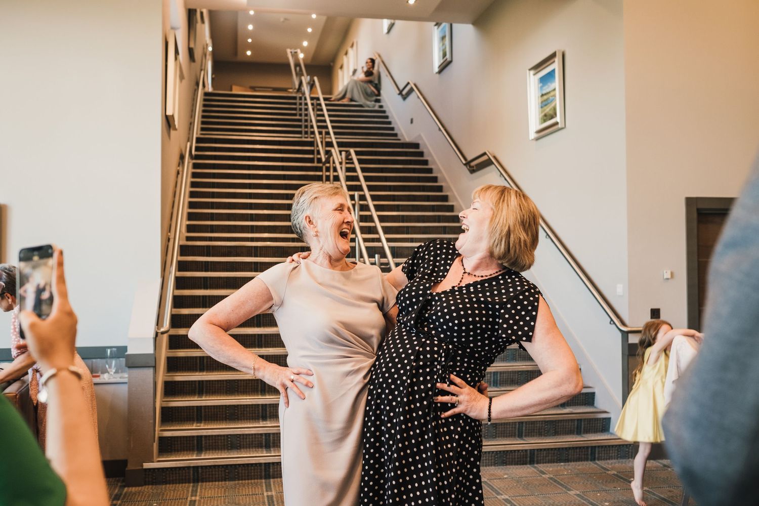 Two women laughing together on a staircase during a celebration.
