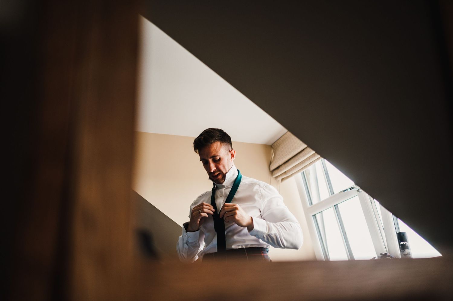 Someone in white adjusts their tie while getting ready by a window.