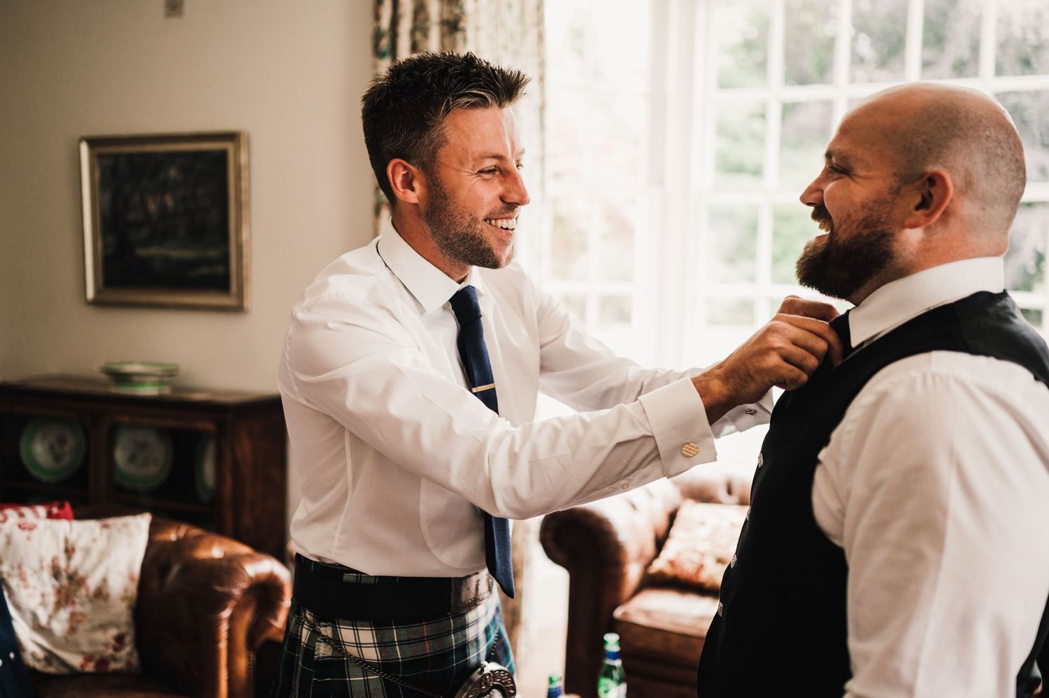 Two men in formal attire helping with wedding preparations.