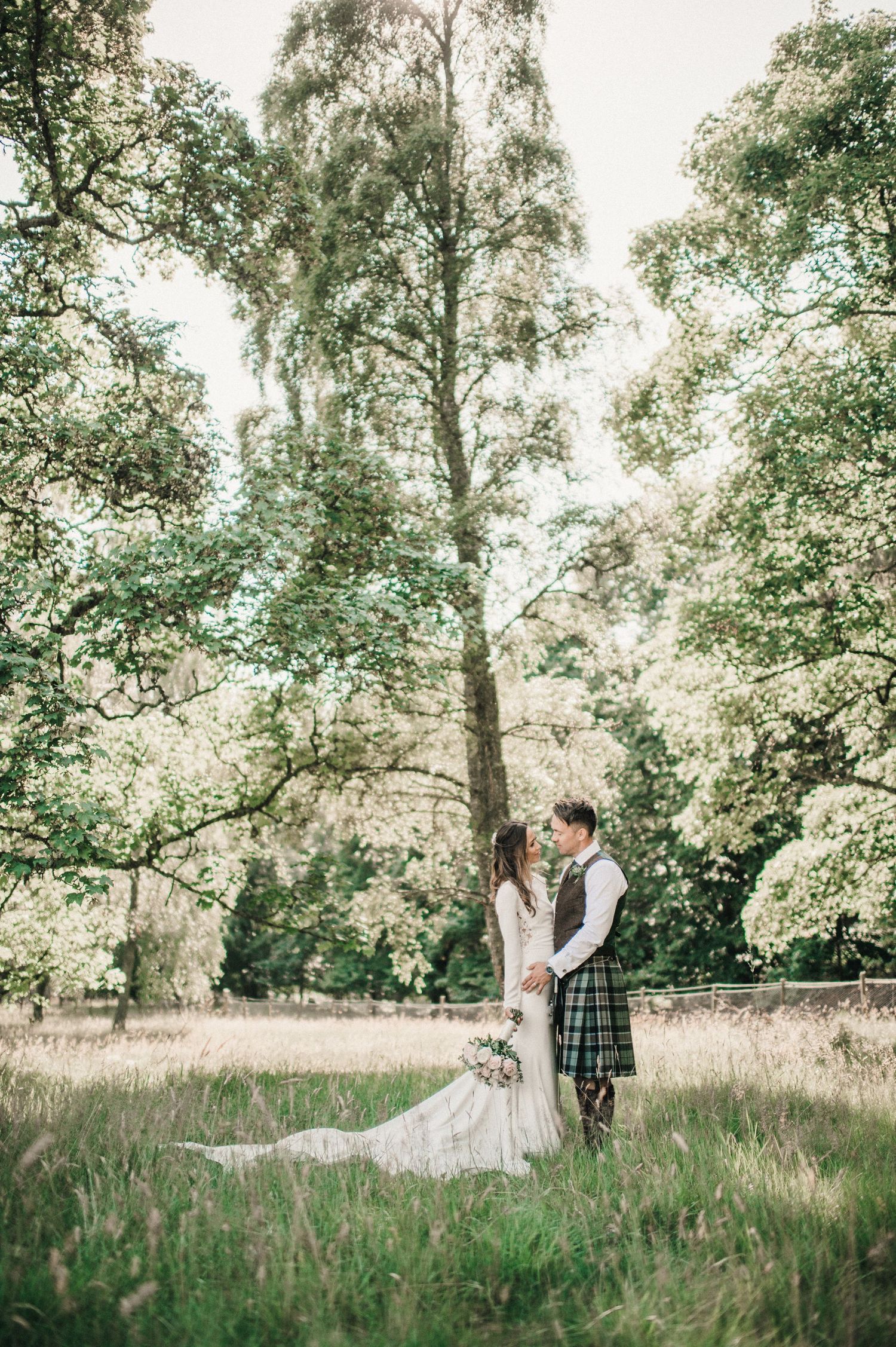 A wedding couple stands together in a serene forest clearing with tall birch trees in the background.