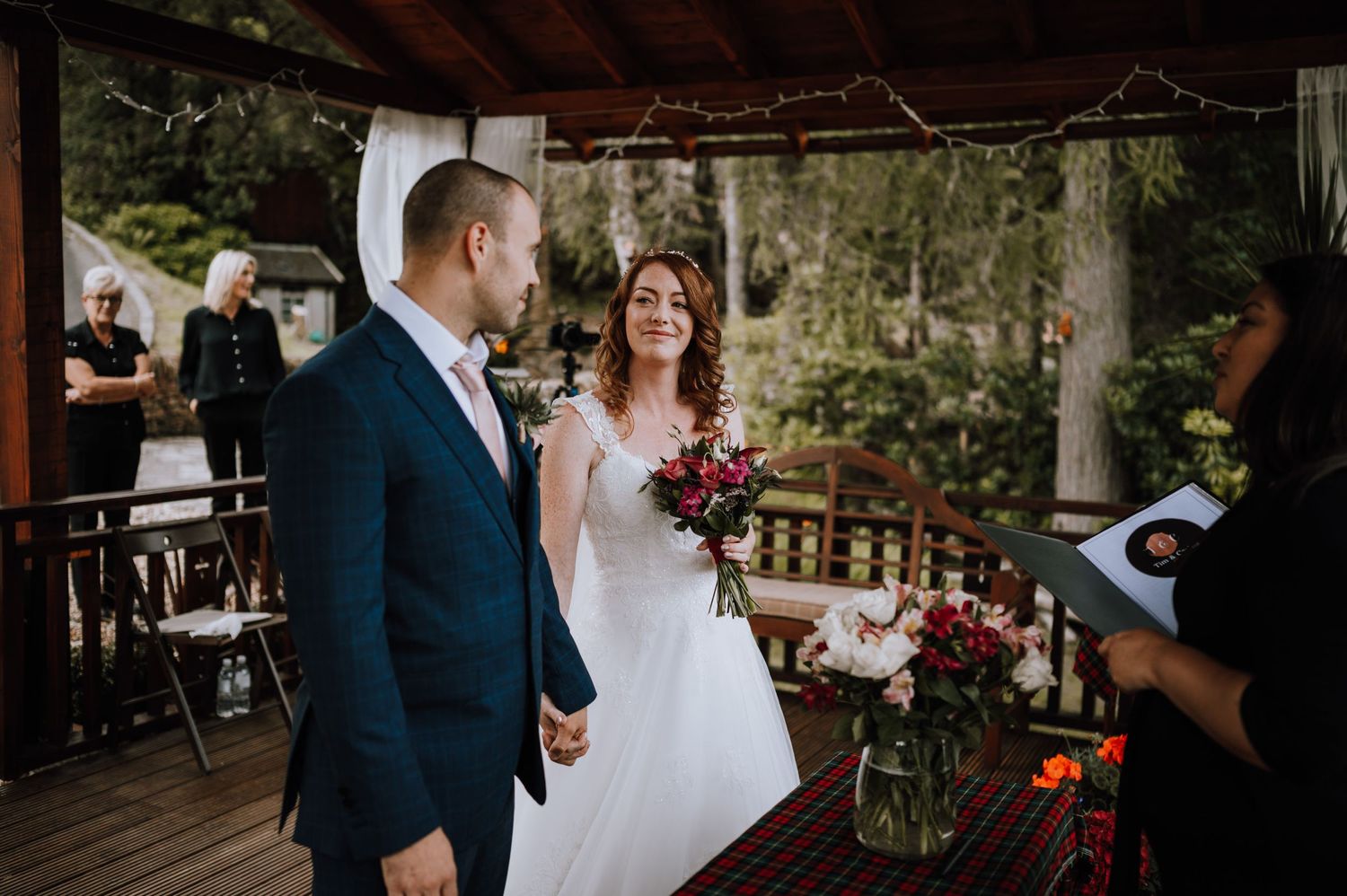 Bride and groom stand under wooden pergola during outdoor ceremony.