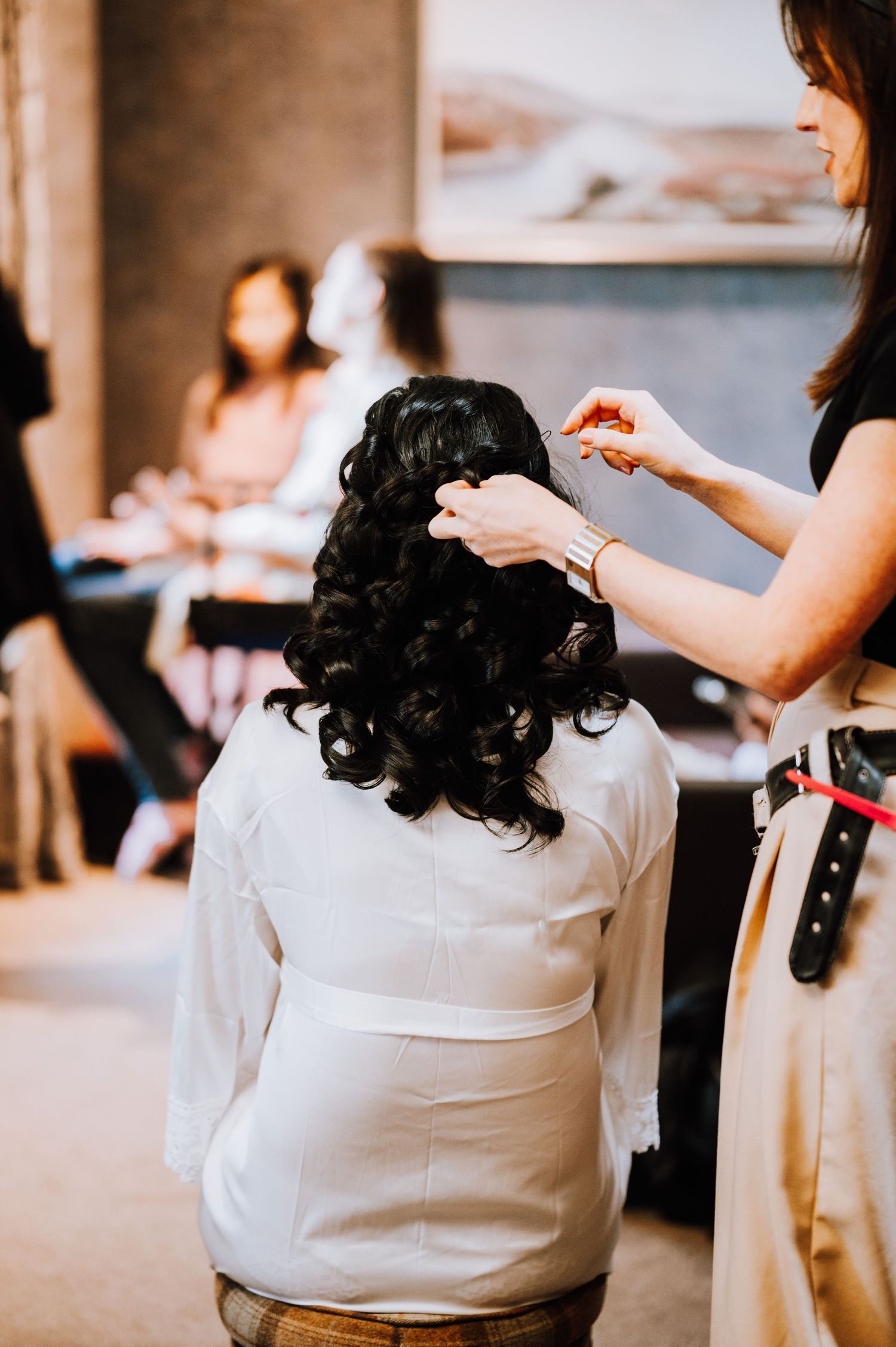 A hairstylist styling dark curled hair during a wedding preparation session.