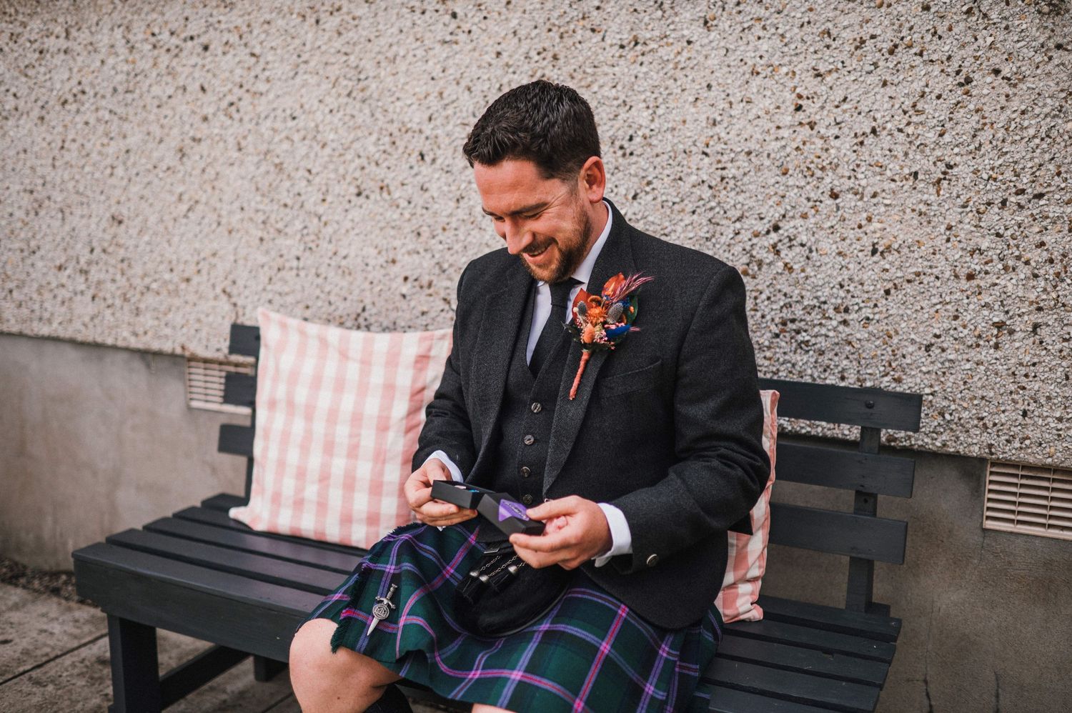 Person holding up a small gift box while wearing traditional Scottish wedding attire.