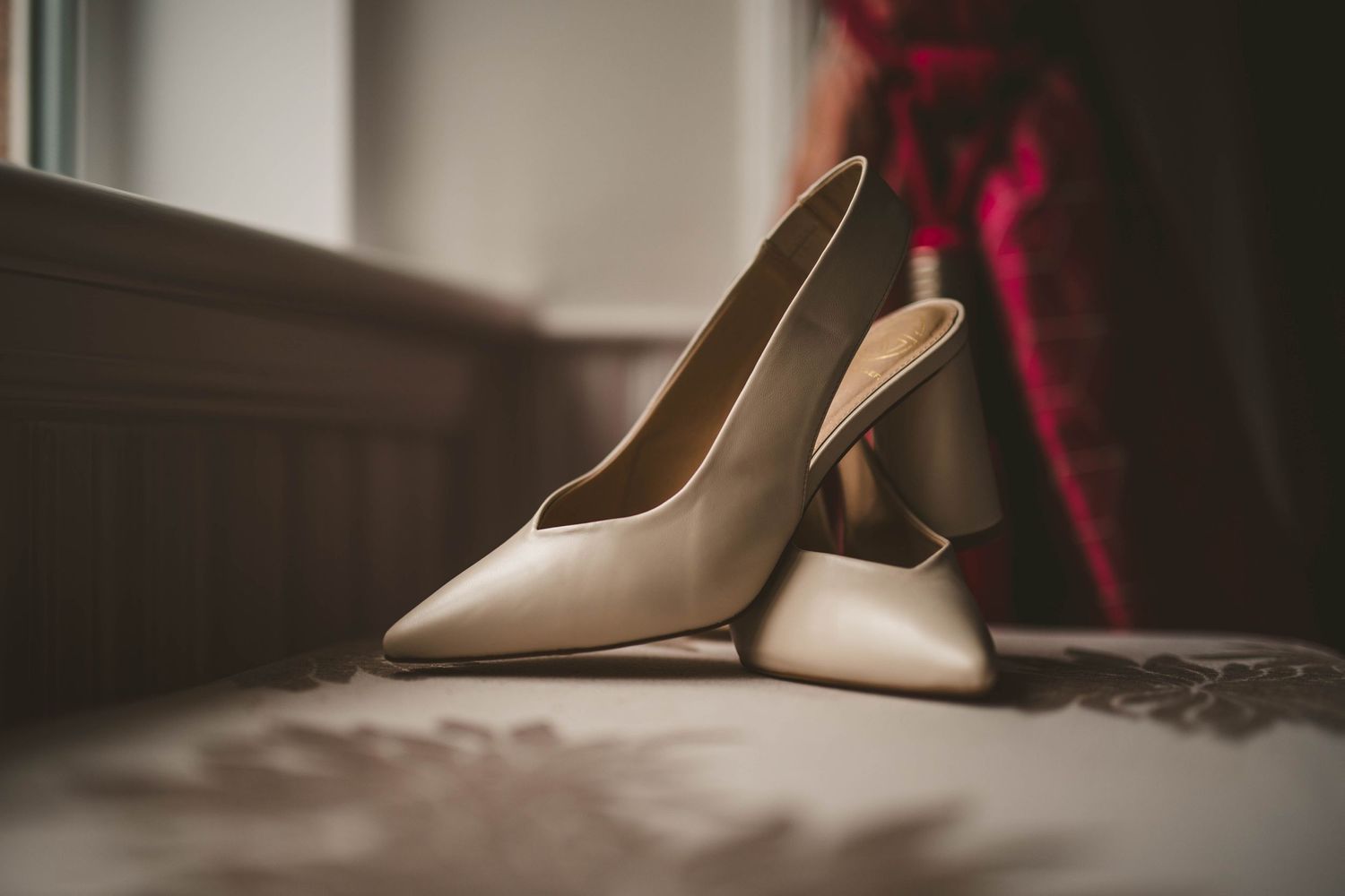 Elegant beige slingback heels sit on a dark surface in soft lighting.