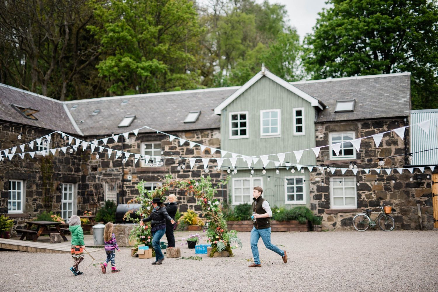 People running across a courtyard decorated with string lights at a stone and mint-colored building venue.