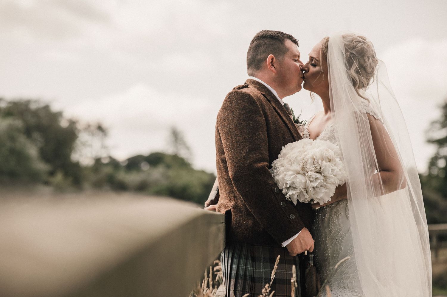 A romantic wedding moment captured with a couple embracing outdoors in traditional Scottish attire.