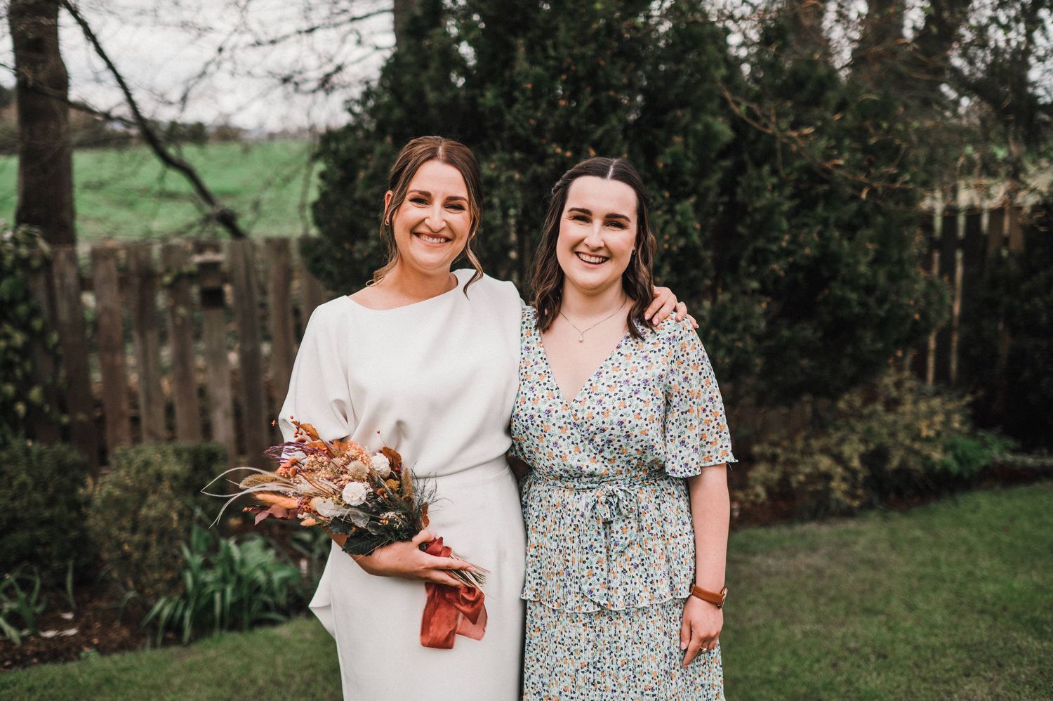 Two women in elegant dresses posing together in a garden setting.