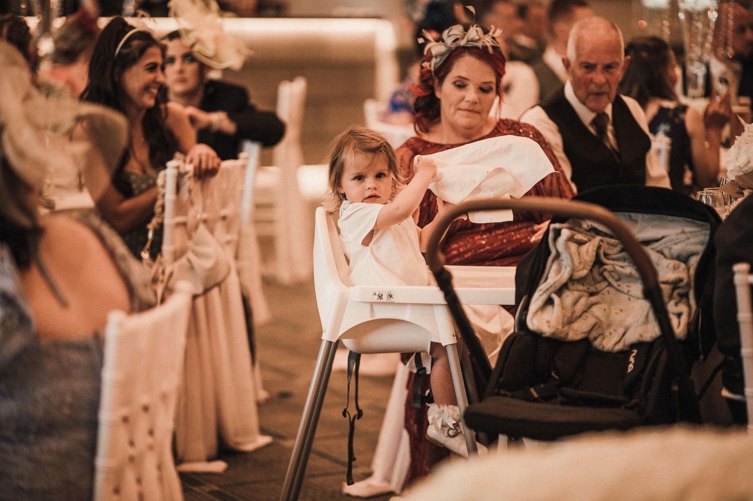 Small child sitting in high chair during formal wedding reception.