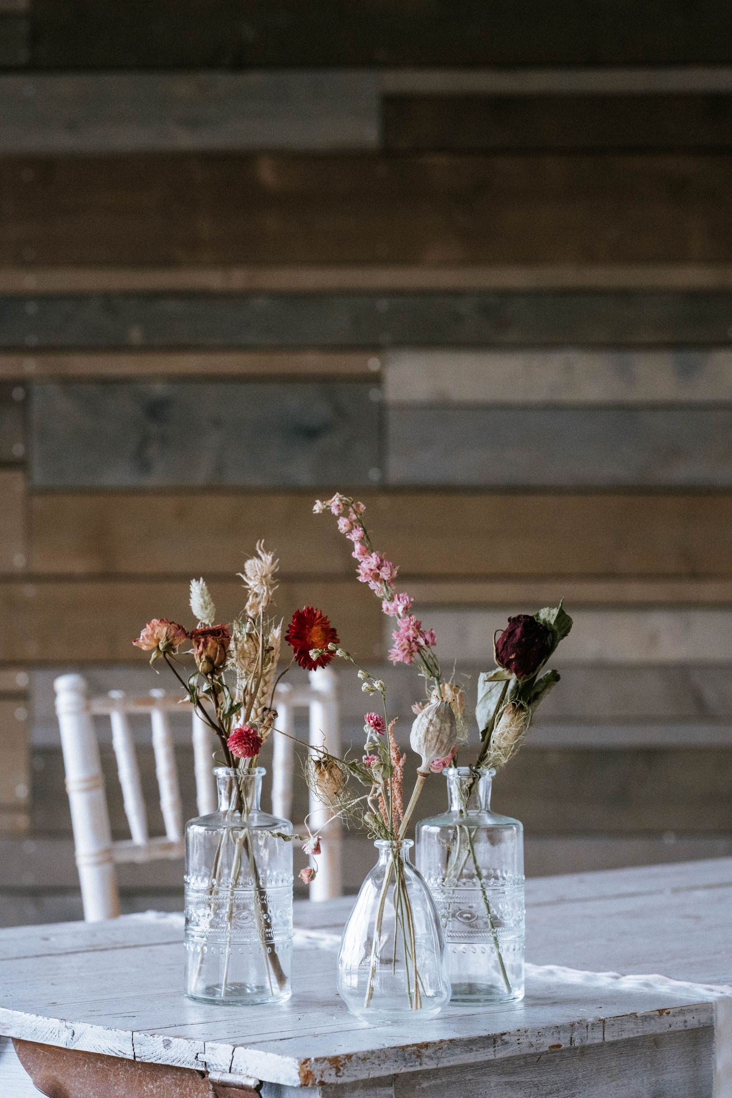 Small glass vases with delicate flowers arranged on a rustic white wooden table.