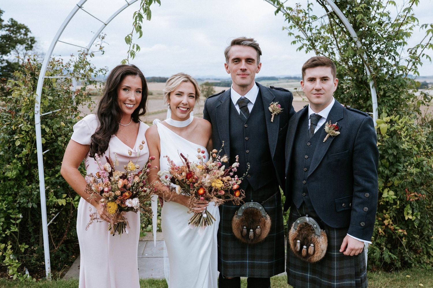Wedding party posing under an arch with autumn flowers and foliage.