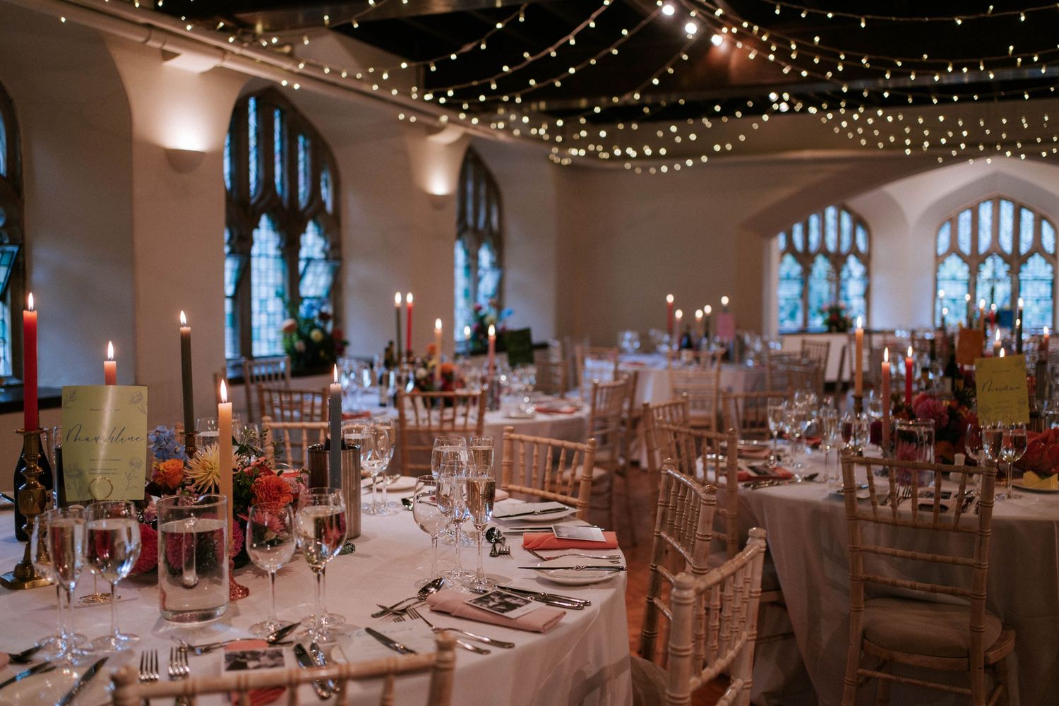 An elegant reception hall with string lights and gothic windows set for a formal dinner.