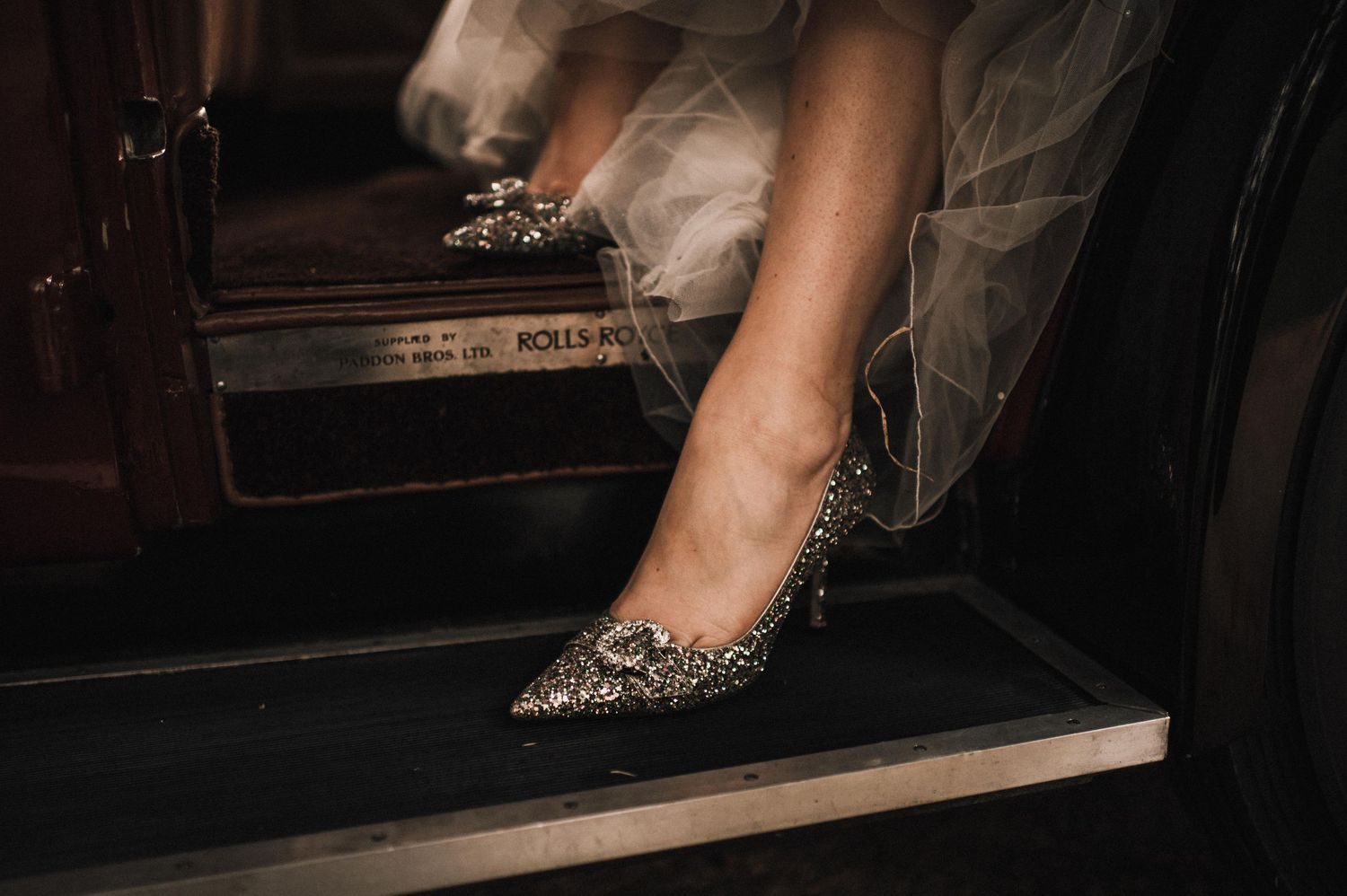 A person in a car wearing sparkly silver high heels with their feet propped up on the dashboard.