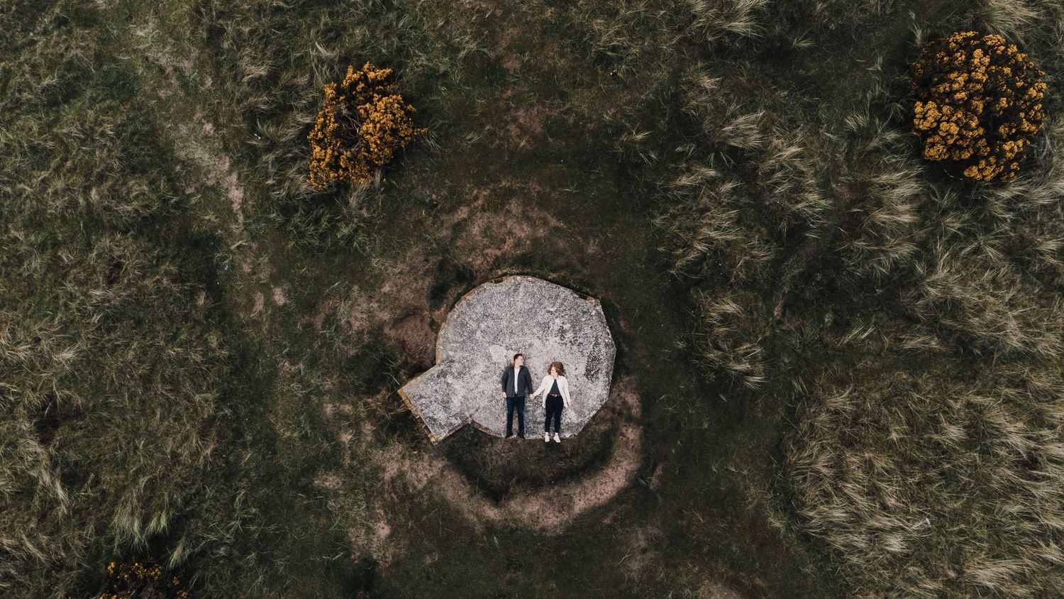 Aerial view of a dark rocky terrain with scattered patches of autumn foliage and small figures visible in the distance.