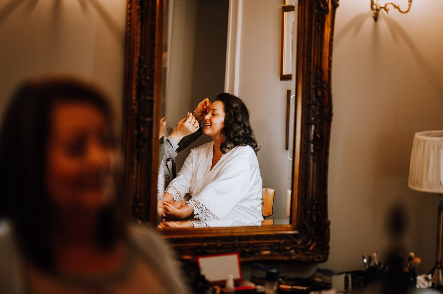 A reflection in an ornate mirror shows someone getting ready while drinking from a glass.