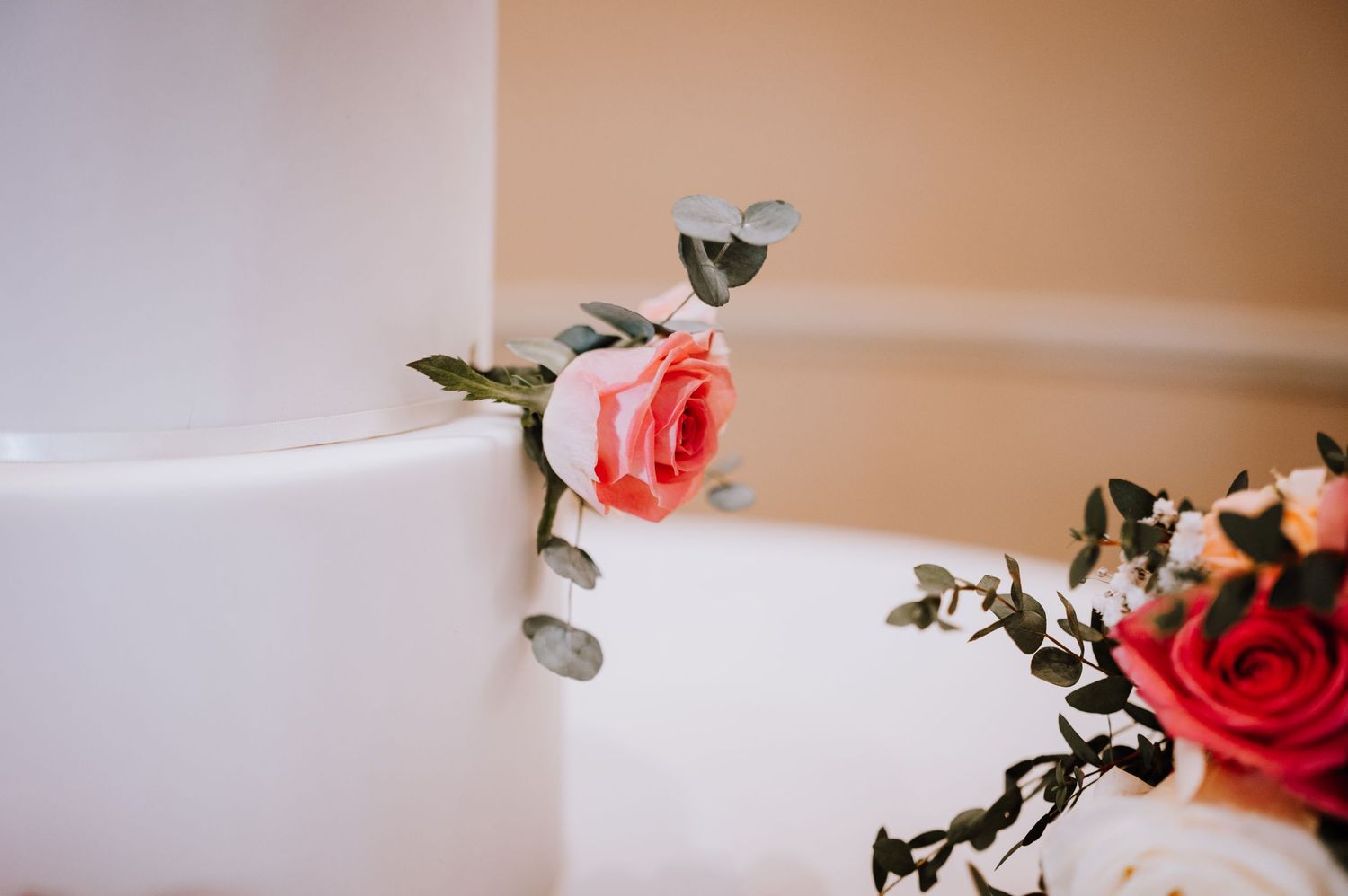 Close-up of a coral rose detail on a white wedding cake.
