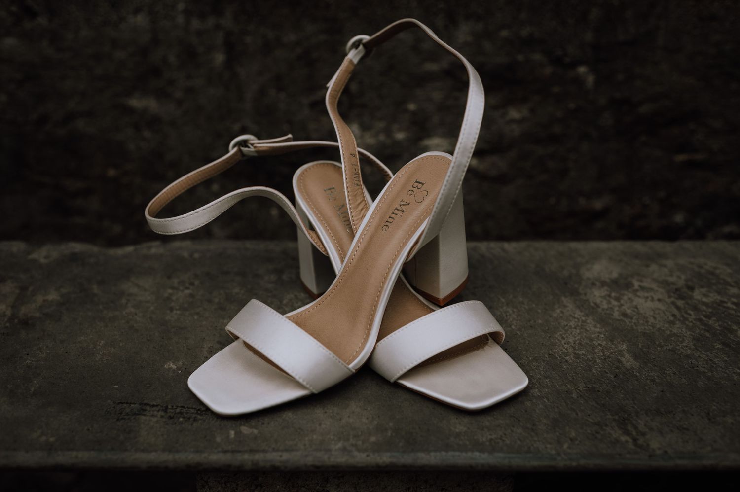 Elegant white leather bridal sandals with block heels displayed on a concrete surface.