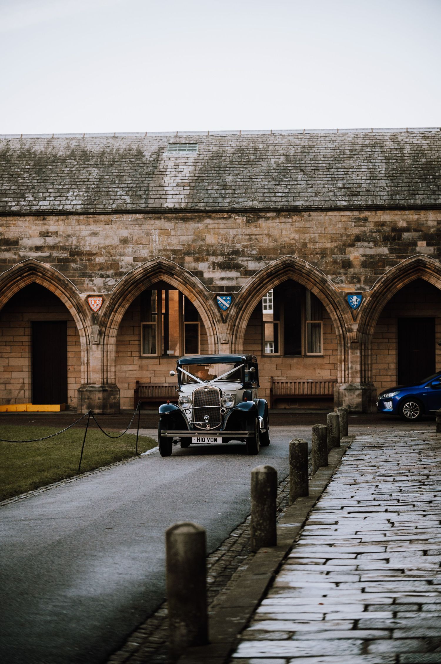 Vintage car parked under Gothic stone arches of historic building.