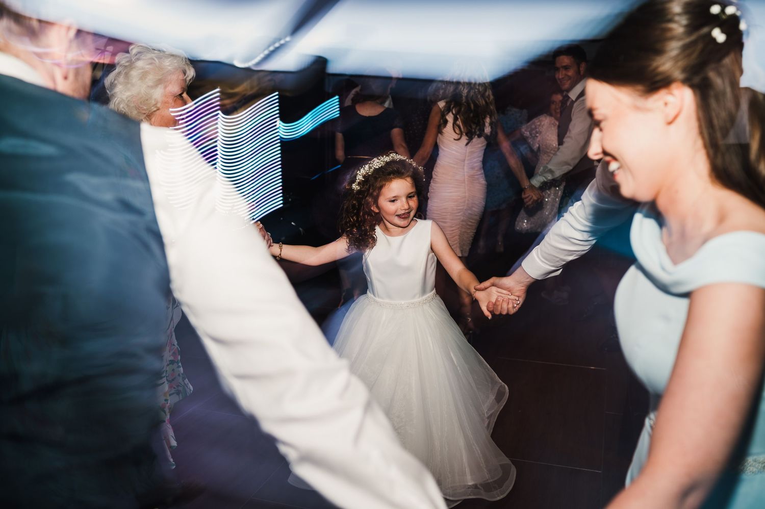 A flower girl in a white dress dances joyfully at a wedding reception celebration.
