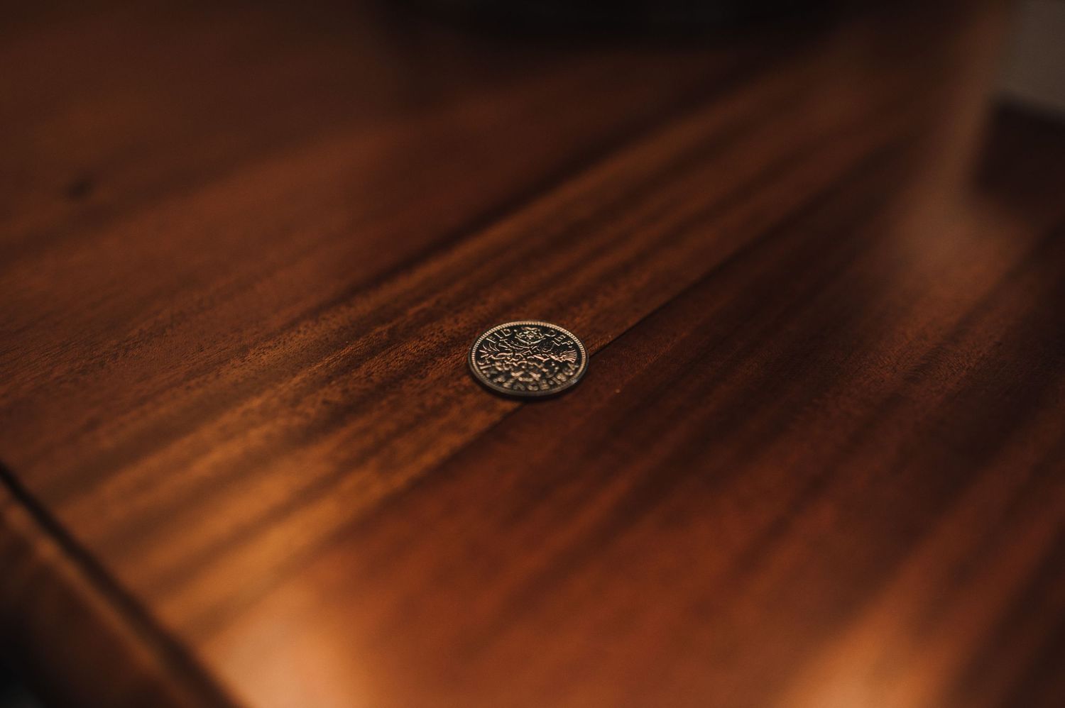 A vintage silver coin placed on dark wooden surface in moody lighting.