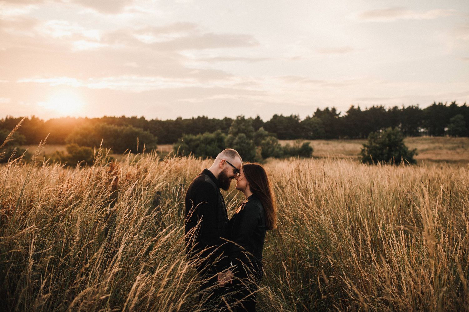 Sunset silhouettes highlight a romantic moment between a couple in a rustic field setting.
