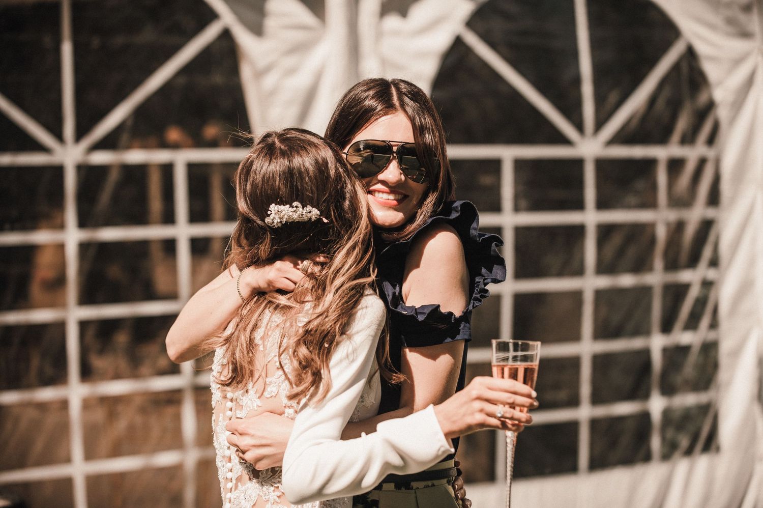 Wedding guests share a joyful moment under a tent structure at an outdoor reception.