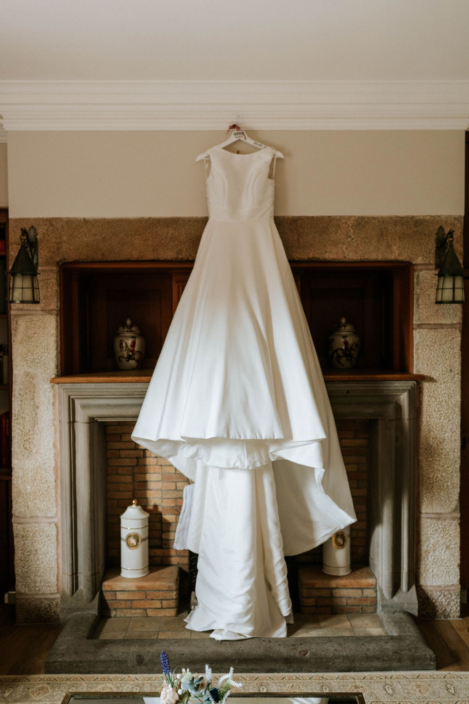 White wedding gown displayed against stone fireplace mantel in classic interior.