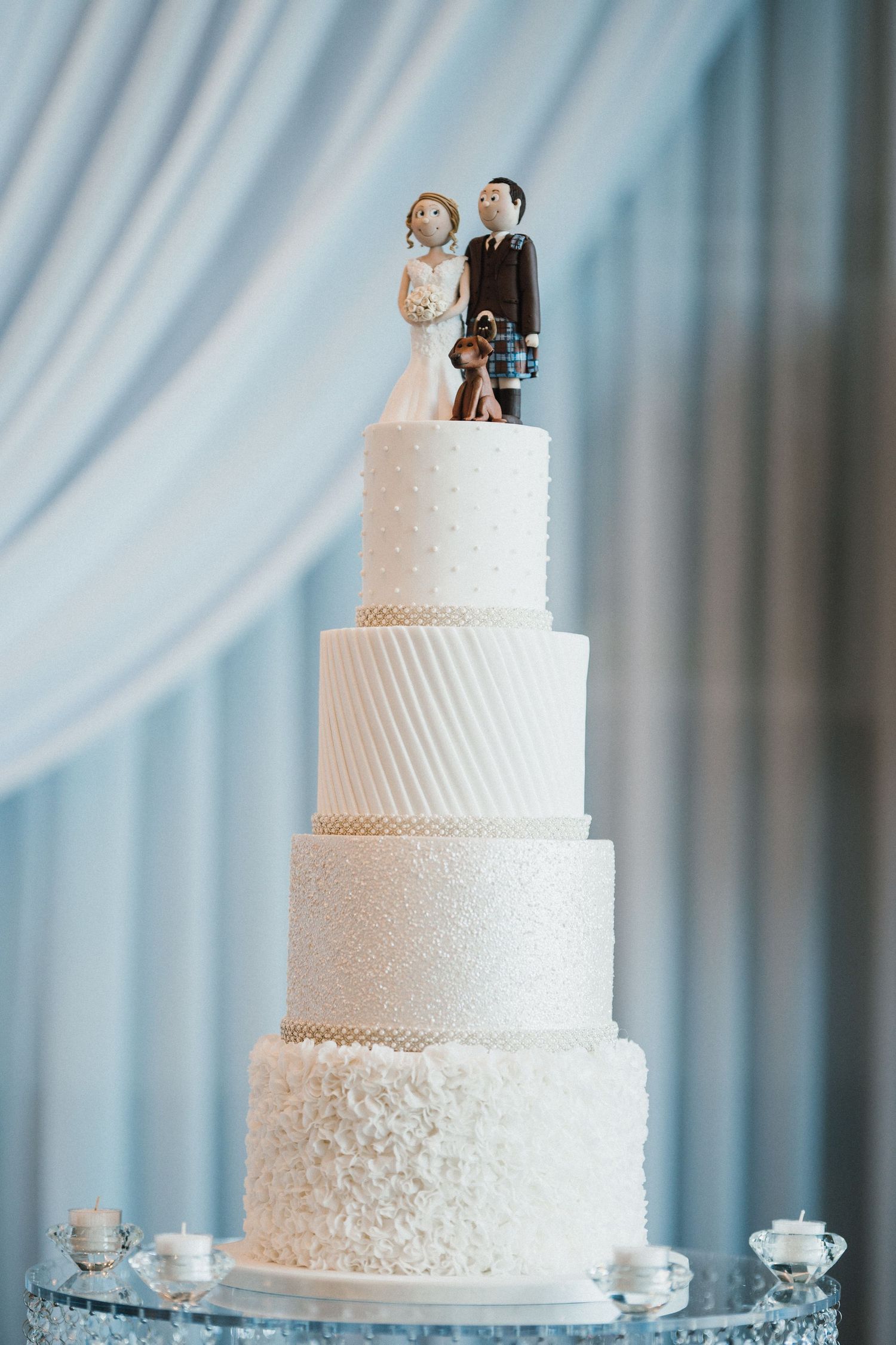 Elegant four-tier white wedding cake with textured layers and decorative topper.