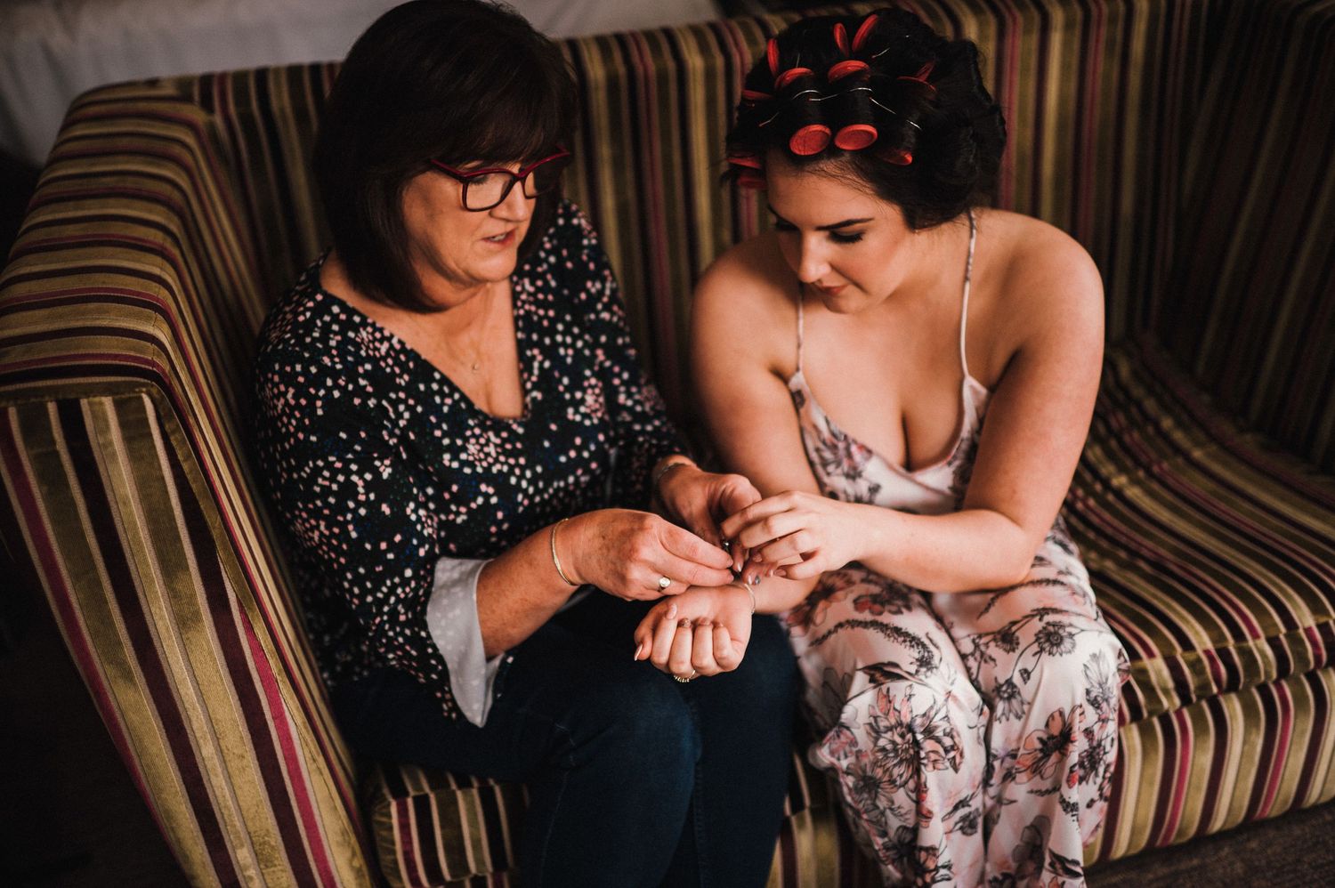 Two people sit on a striped couch looking at something on their phones together.
