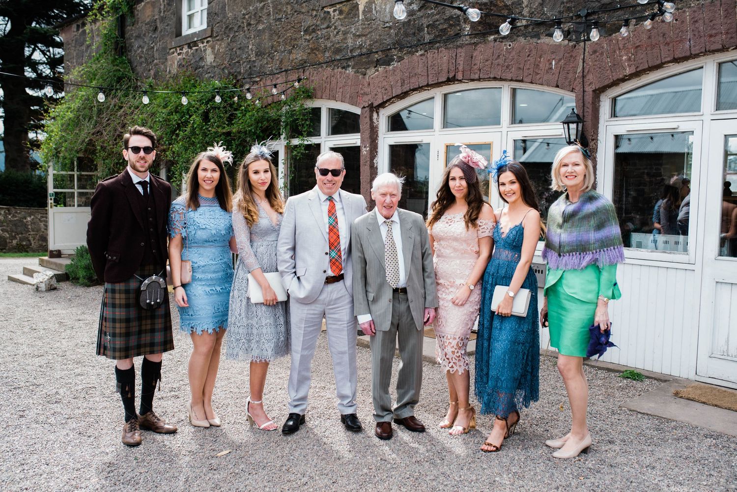 Wedding party group photo with mix of formal attire including kilts and summer dresses.