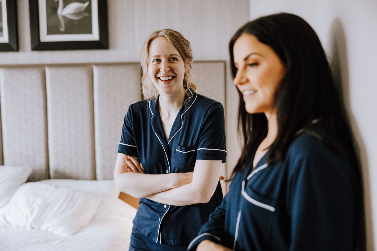Two people in navy silk pajamas share a joyful moment in a bedroom setting.