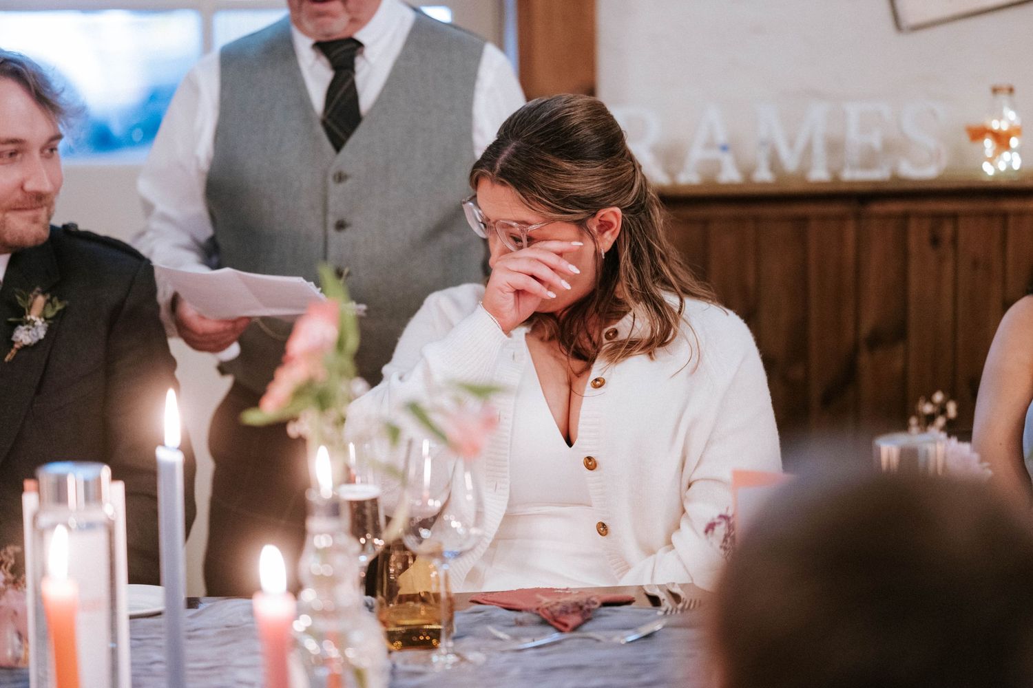 Wedding guests seated at long tables with candlelight during an indoor reception celebration.
