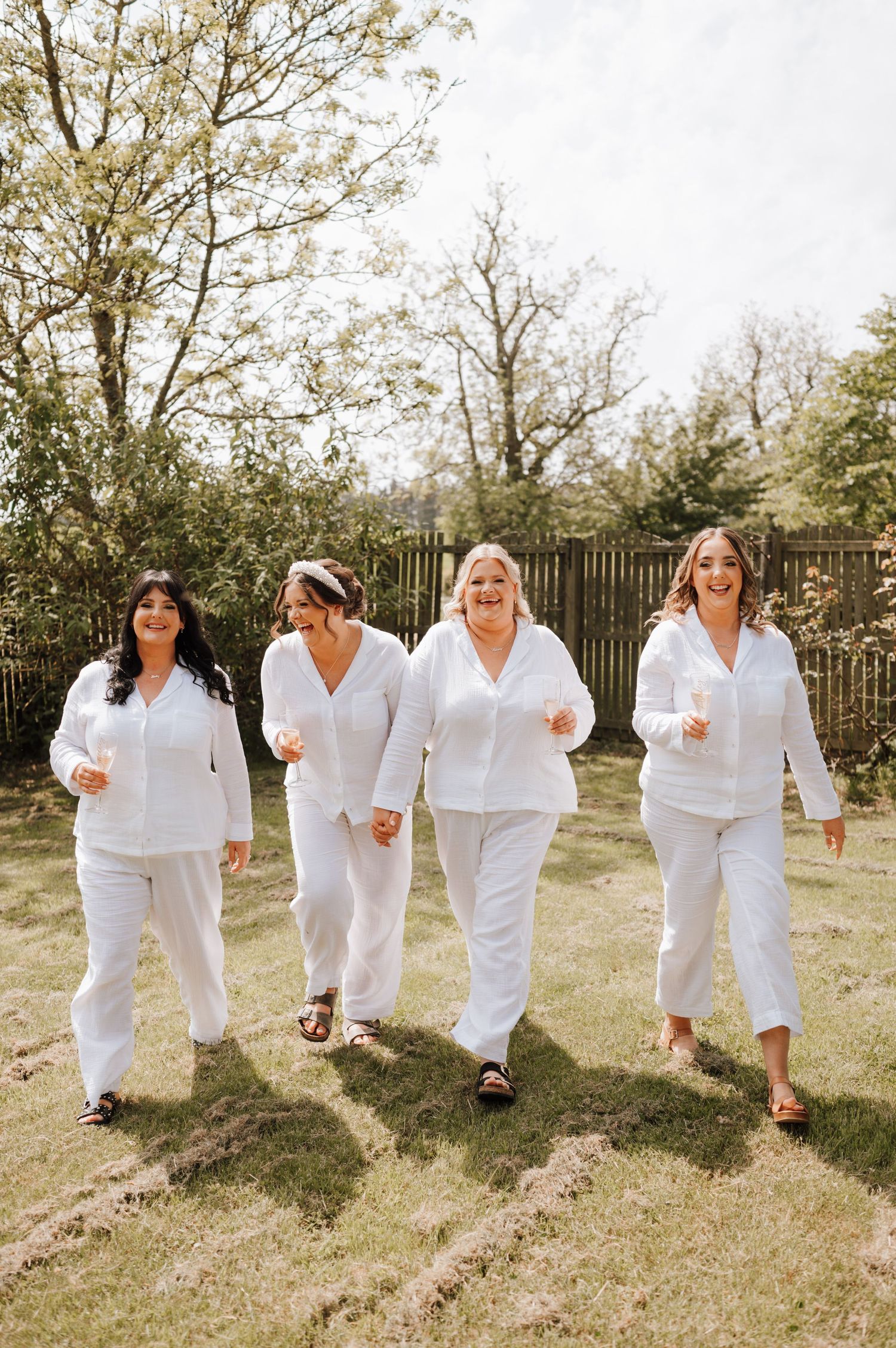 Four people walking together in matching white outfits on a sunny lawn.