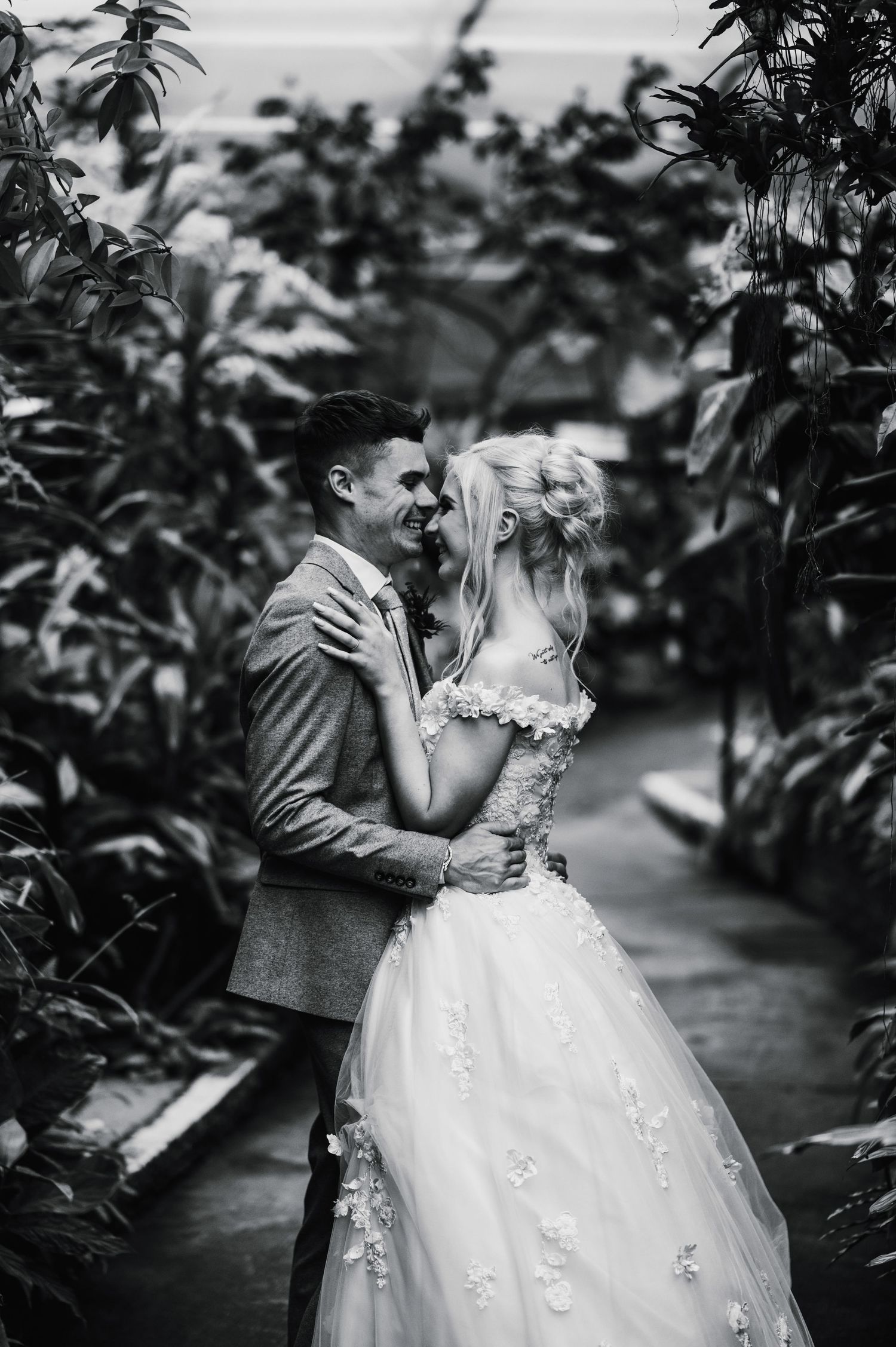 Black and white romantic wedding photo in a greenhouse surrounded by plants.