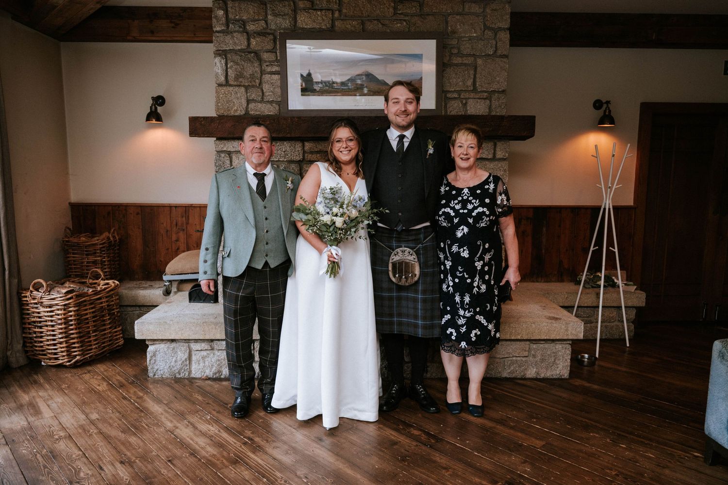 A wedding party poses in front of a rustic stone fireplace with wooden accents and gift baskets.