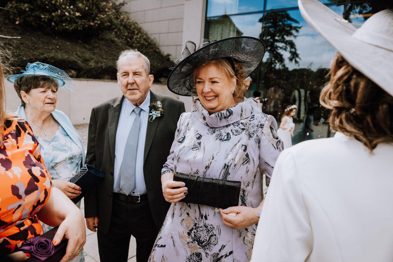 Wedding guests gathered outside in formal attire and decorative hats.