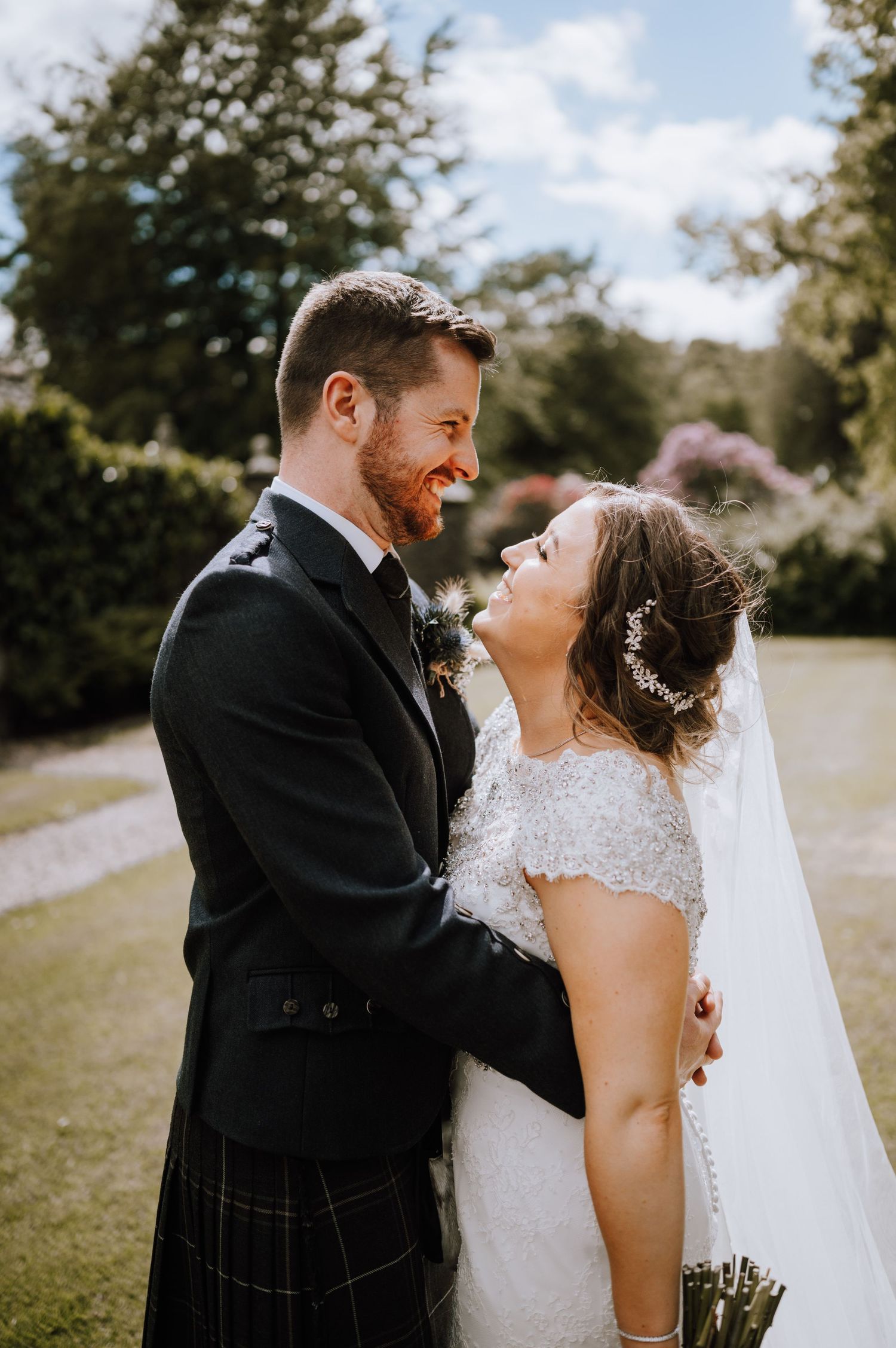 A joyful wedding couple laugh together in their traditional Scottish and white wedding attire.