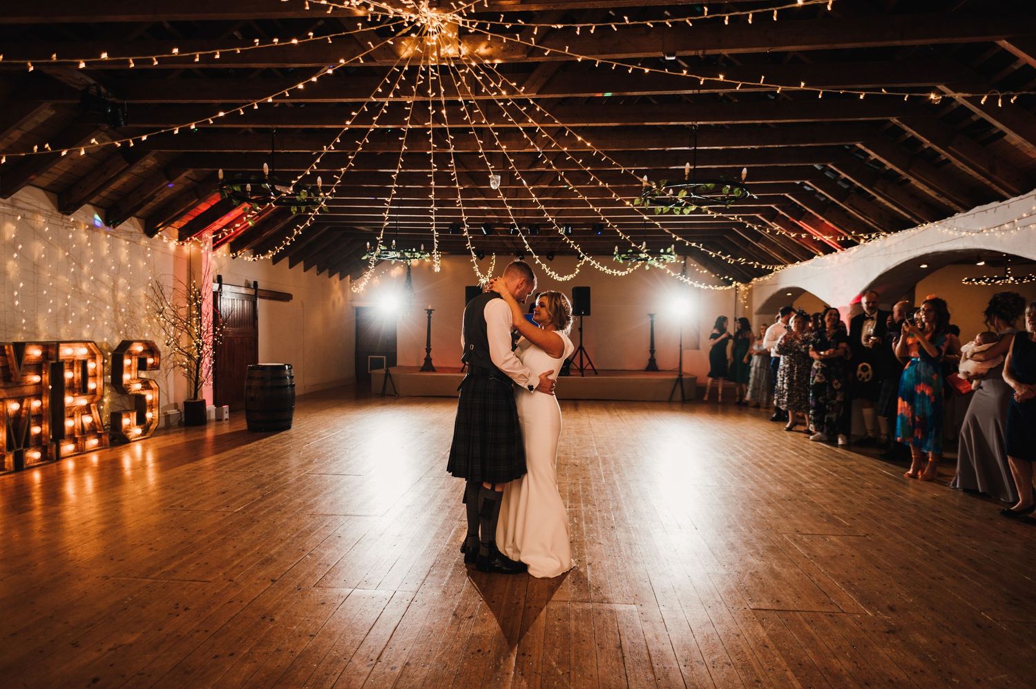 A couple shares their first dance under twinkling string lights in an elegant reception venue.
