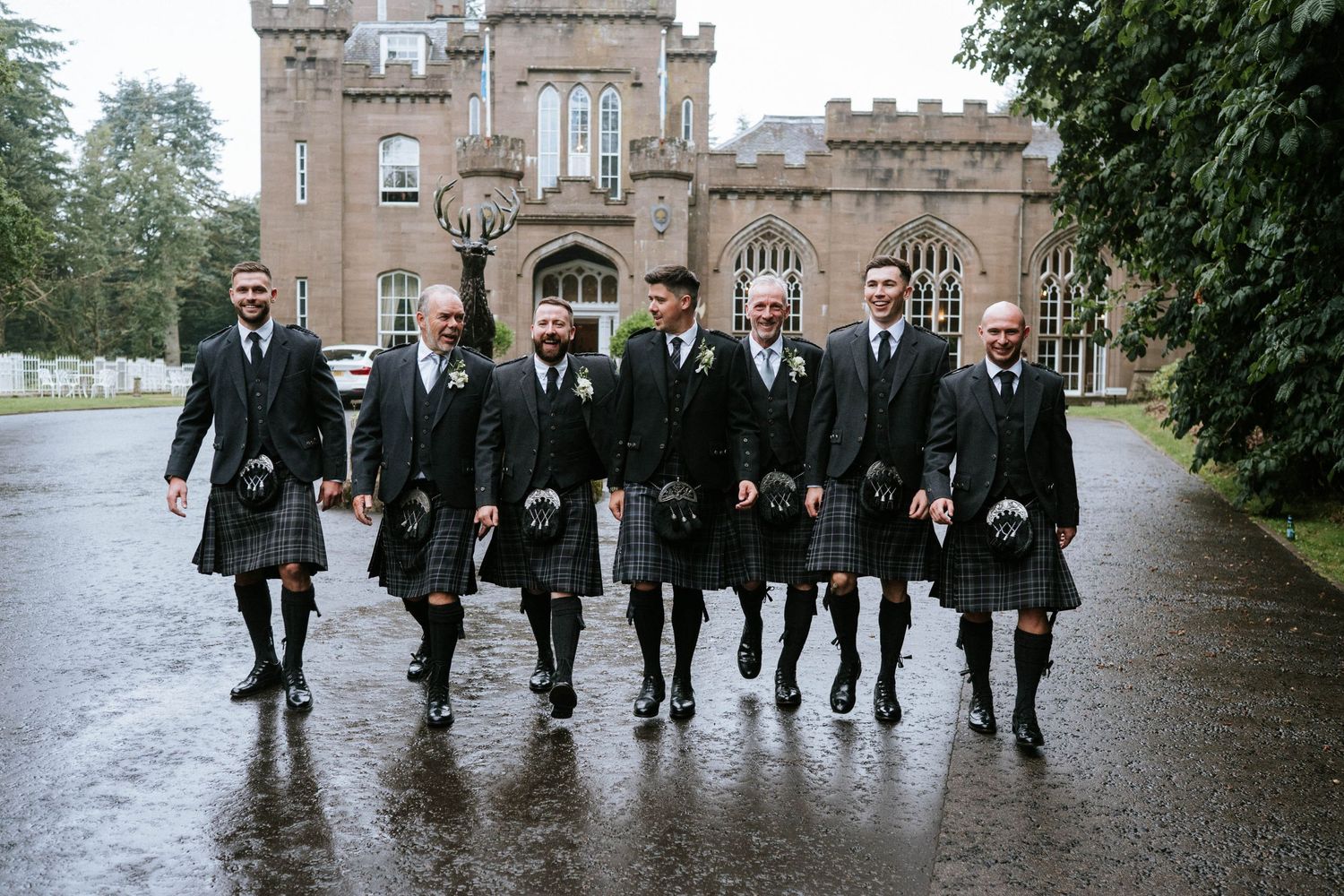 Wedding party walking together in the rain outside a grand stone building.