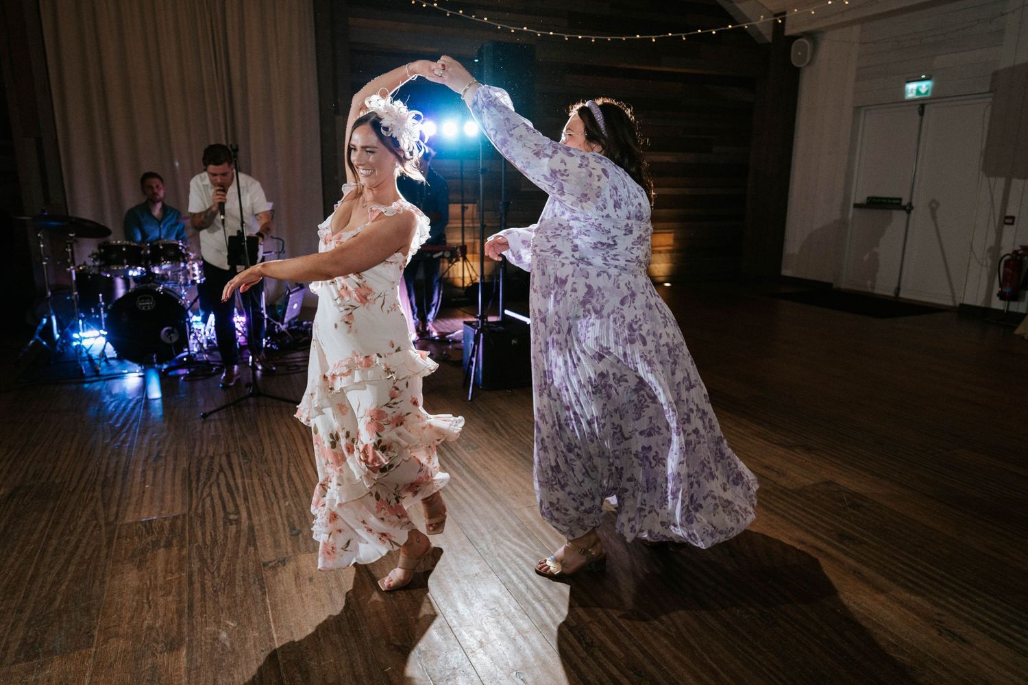 Couples dancing at wedding reception under twinkling lights on wooden dance floor.