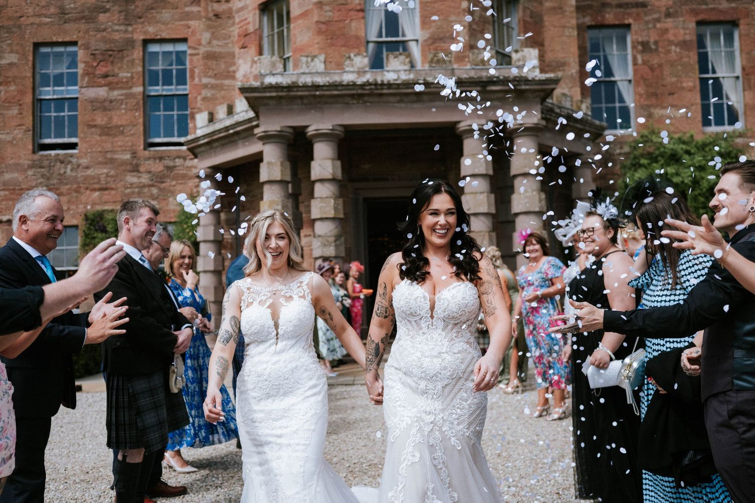 Fasque Castle Wedding Photography. Wedding celebration outside historic brick building as guests shower couple with confetti.