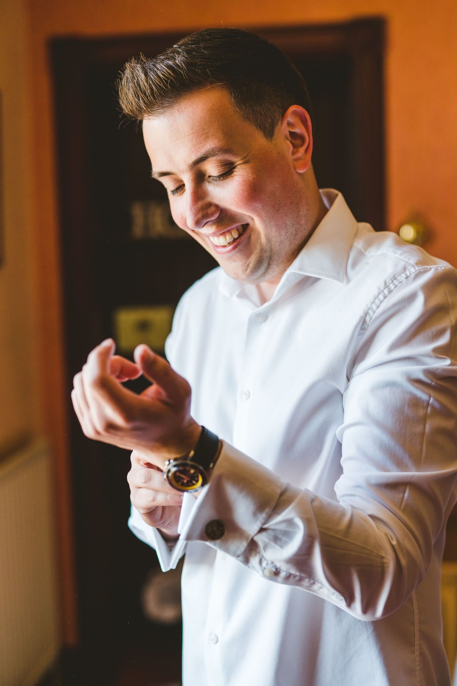 Person in white dress shirt adjusting cufflinks during wedding preparations.