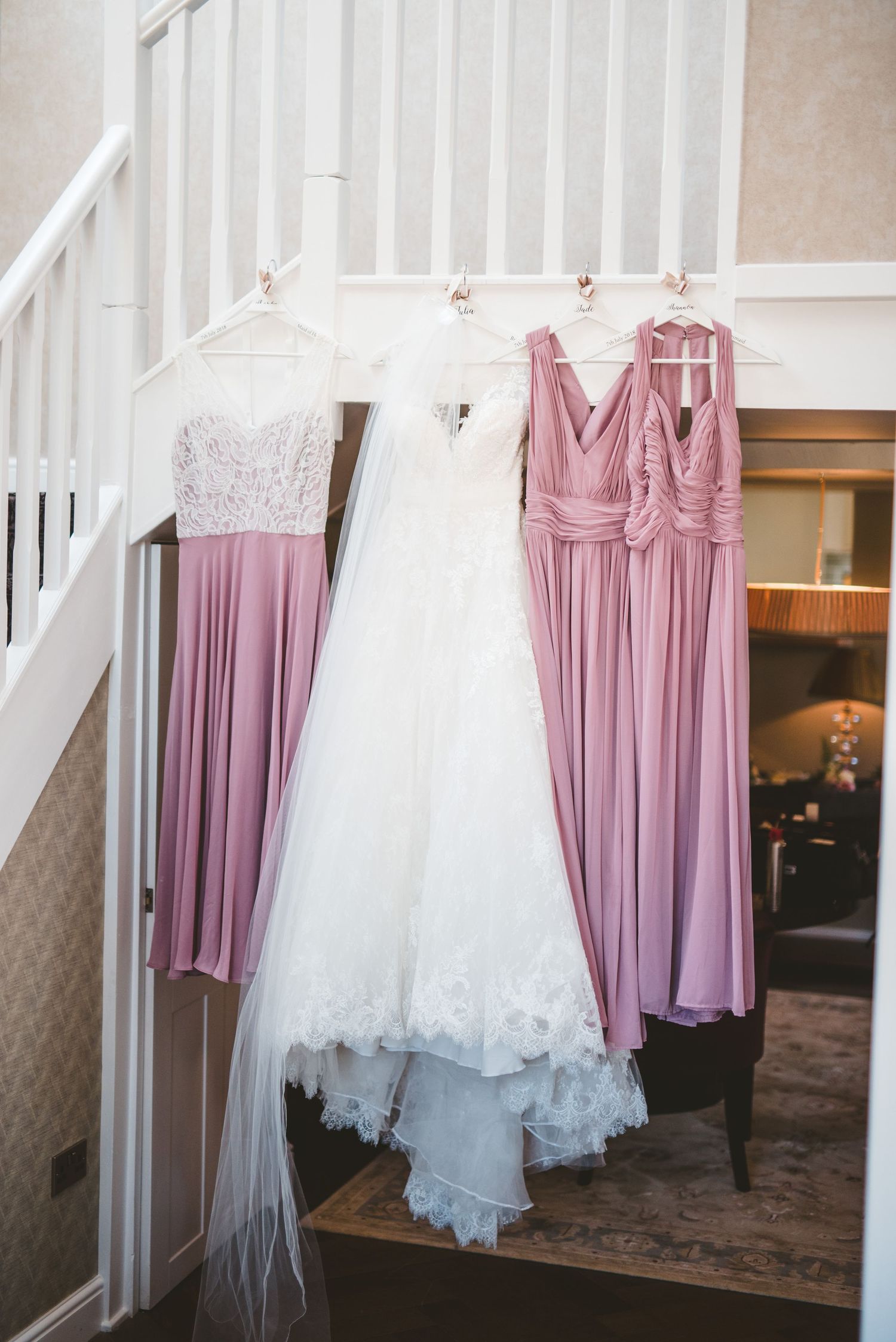 Wedding dresses in white and bridesmaid dresses in dusty rose hang elegantly against a white backdrop.