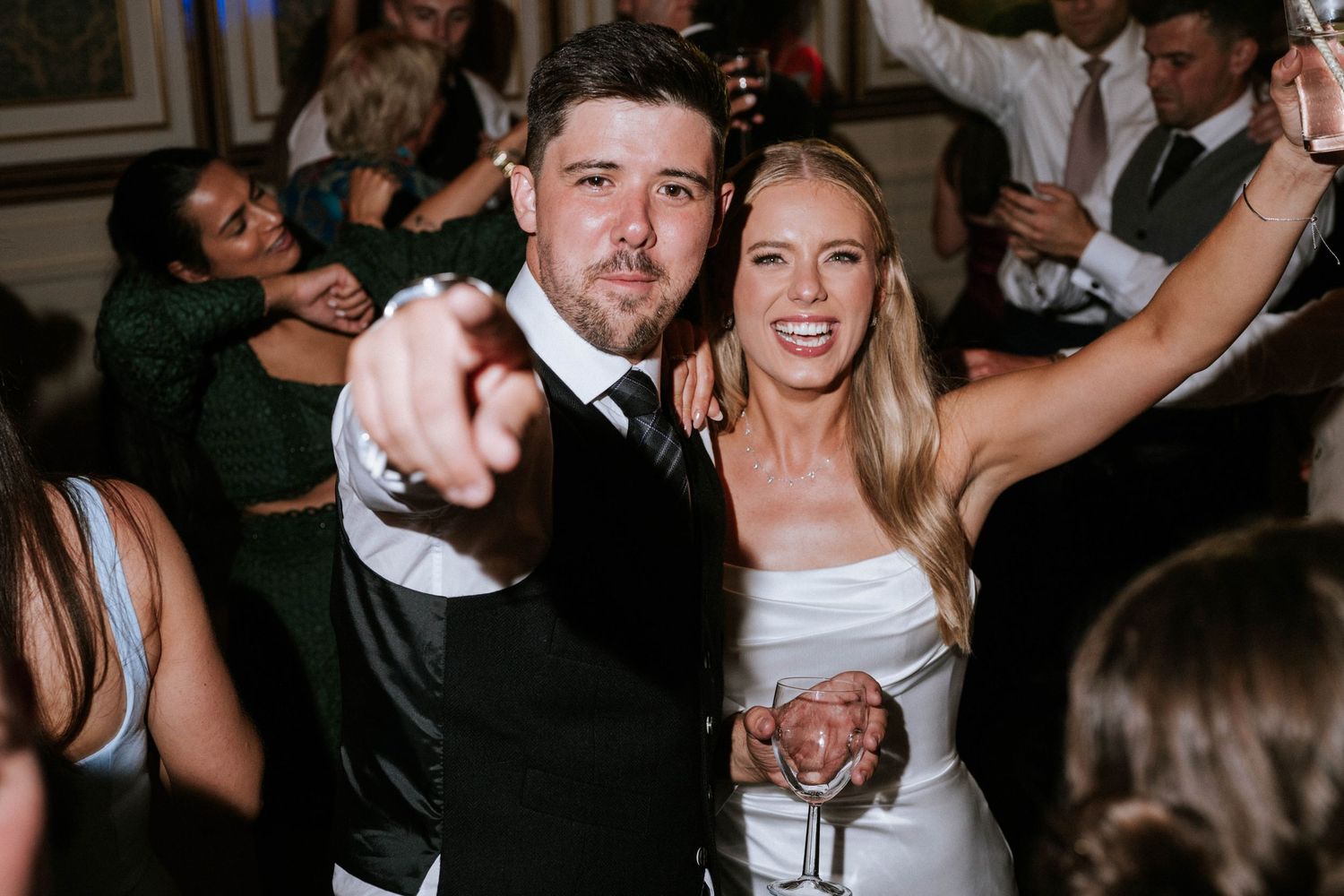 Wedding reception dance party with guests celebrating in a dimly lit venue.