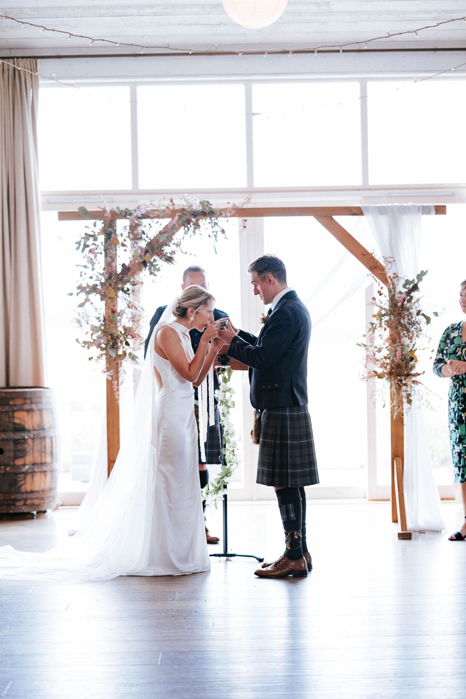 A couple shares their first look in a bright, airy venue with wooden barrels and white curtains.